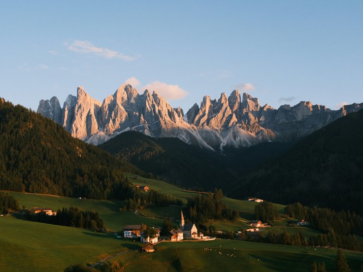 Scoprire l’Alto Adige da Maranza: giornate in montagna davanti alla porta ed escursioni a Bressanone, in Val Pusteria e nelle Dolomiti. Pianifica la tua vacanza.. Luce del tramonto sulle Dolomiti sopra una valle verde con case sparse